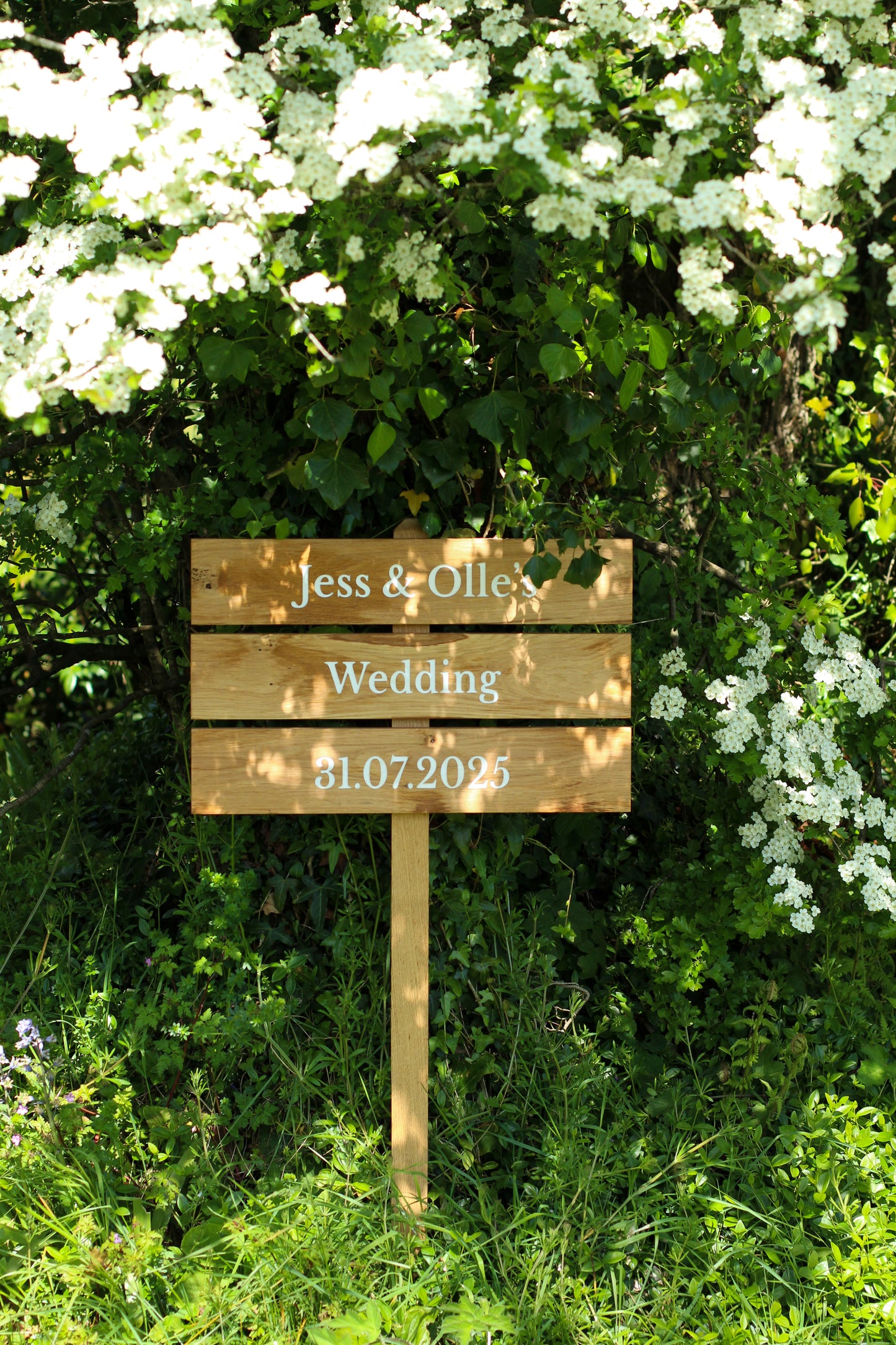 Wooden wedding sign in a garden setting with white flowers.