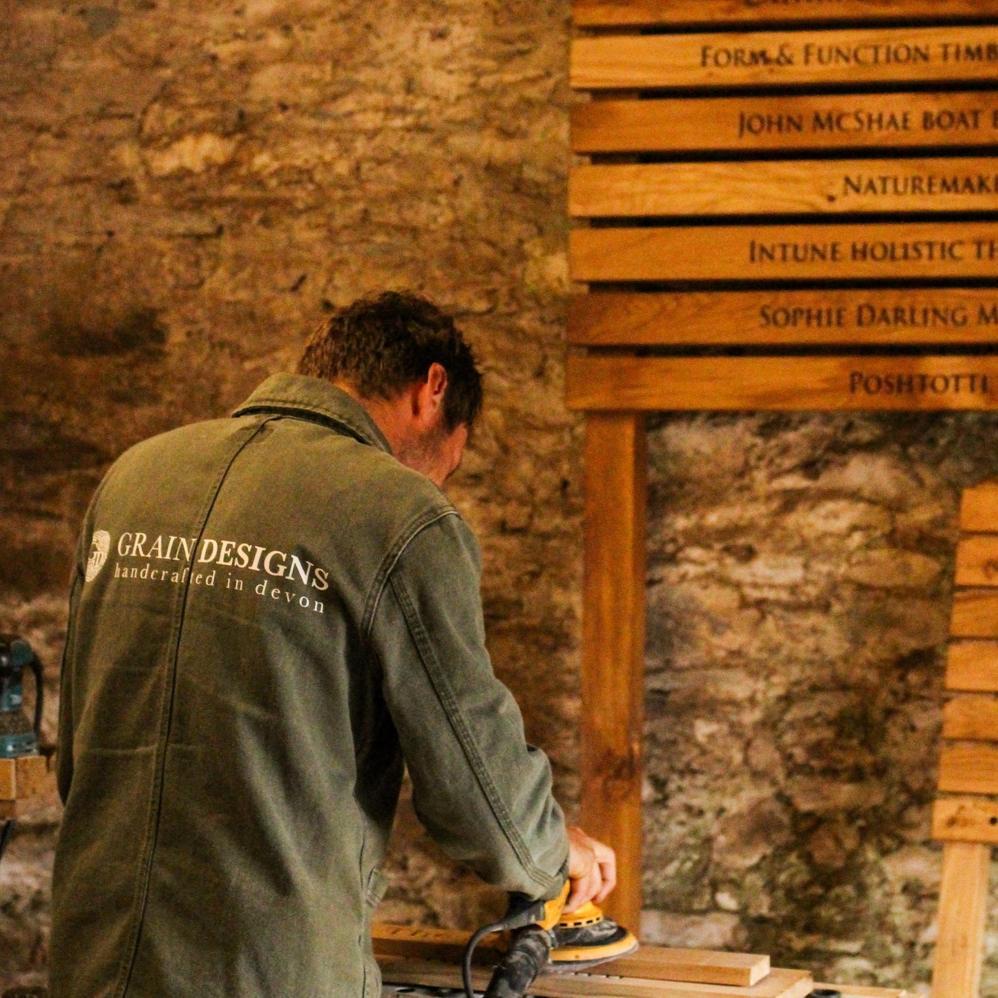 Man working on wooden furniture with a rustic stone wall background