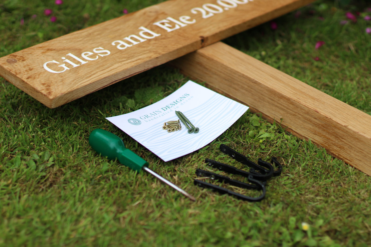 Wooden garden tool with engraved names, screwdriver, and screws on grass