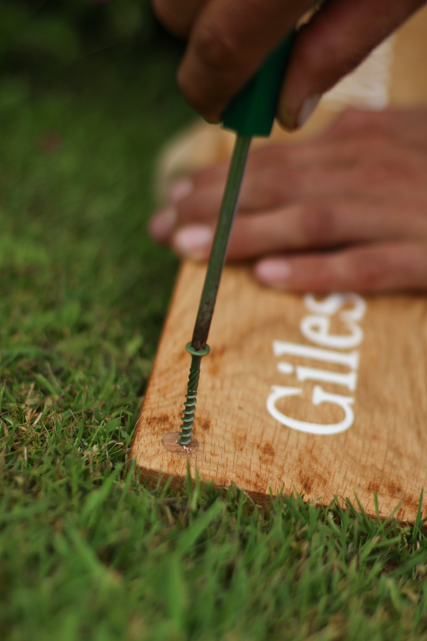 Person using a screwdriver on a wooden block with 'Giles' branding in a grassy area