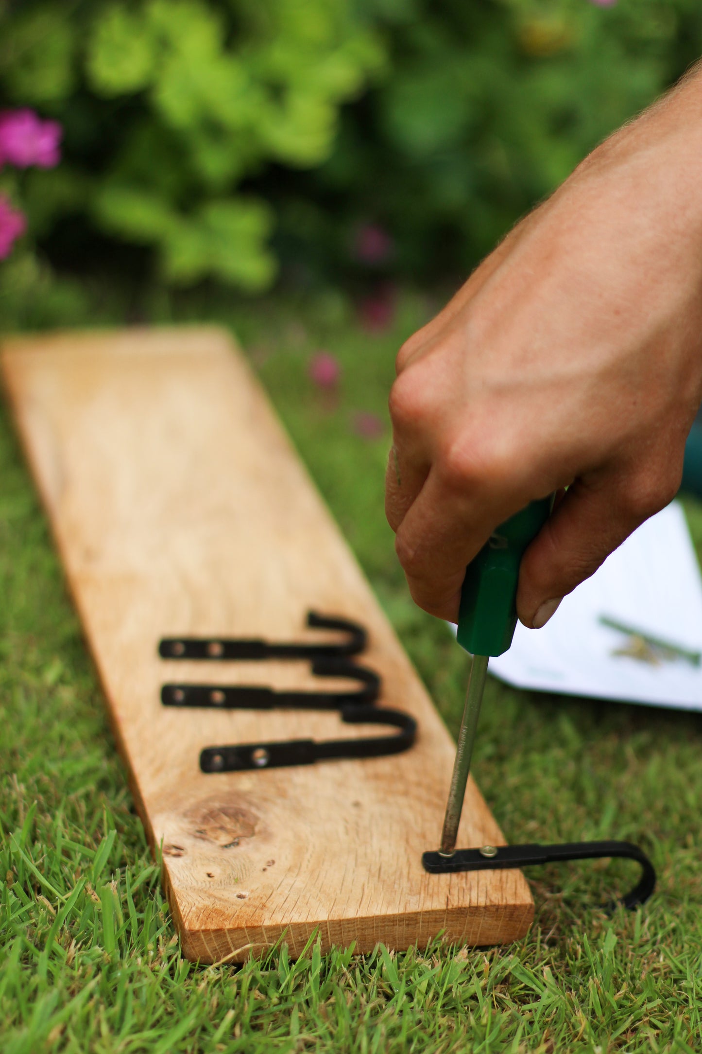 Hand using a tool on a wooden board with metal hooks on a grassy background