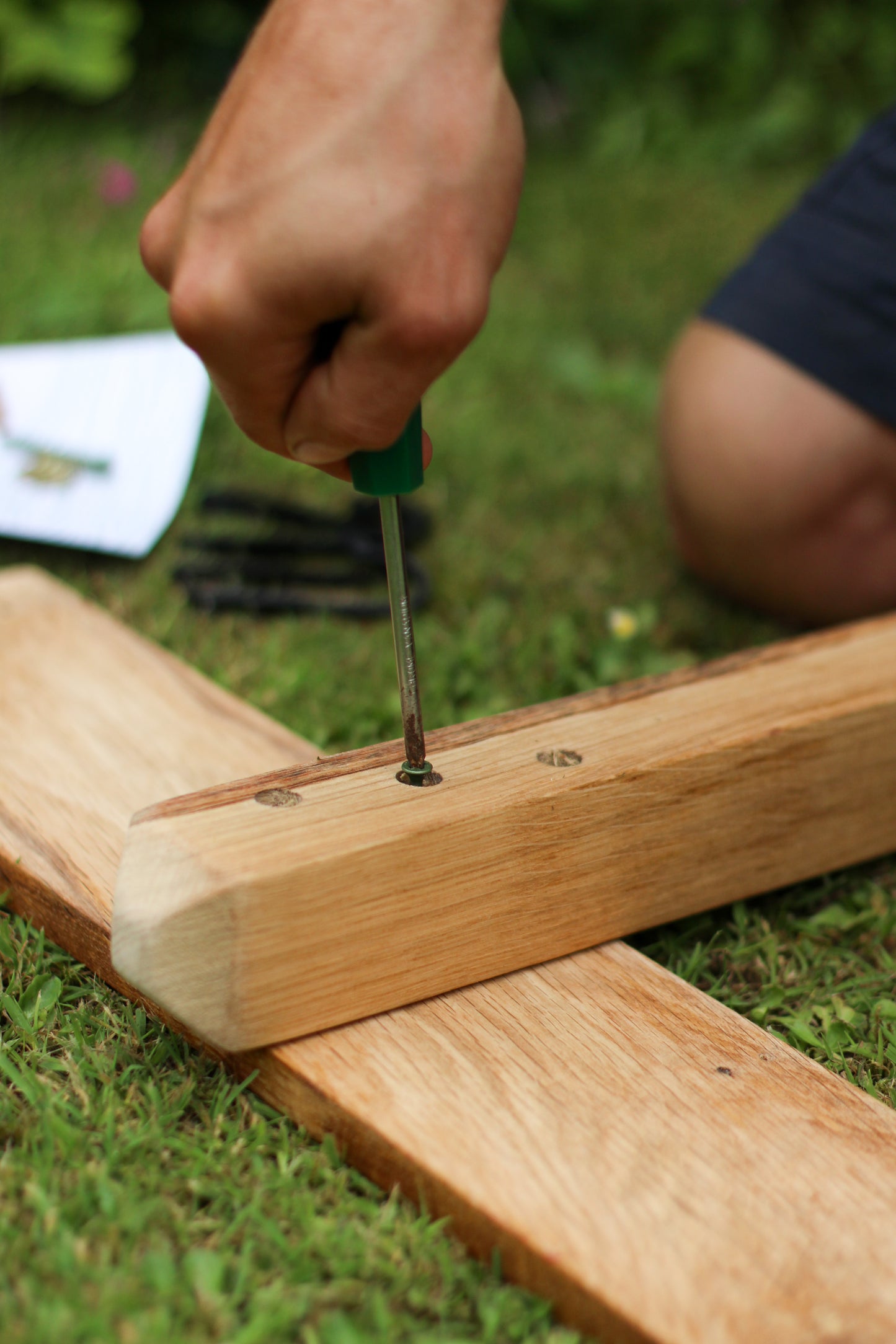 Hand using a screwdriver to secure wooden planks on a grassy surface