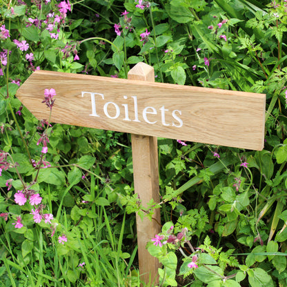 A wooden wedding sign with 'Jess & Olle's Wedding 31.07.2021' engraved on it, set against a backdrop of greenery.