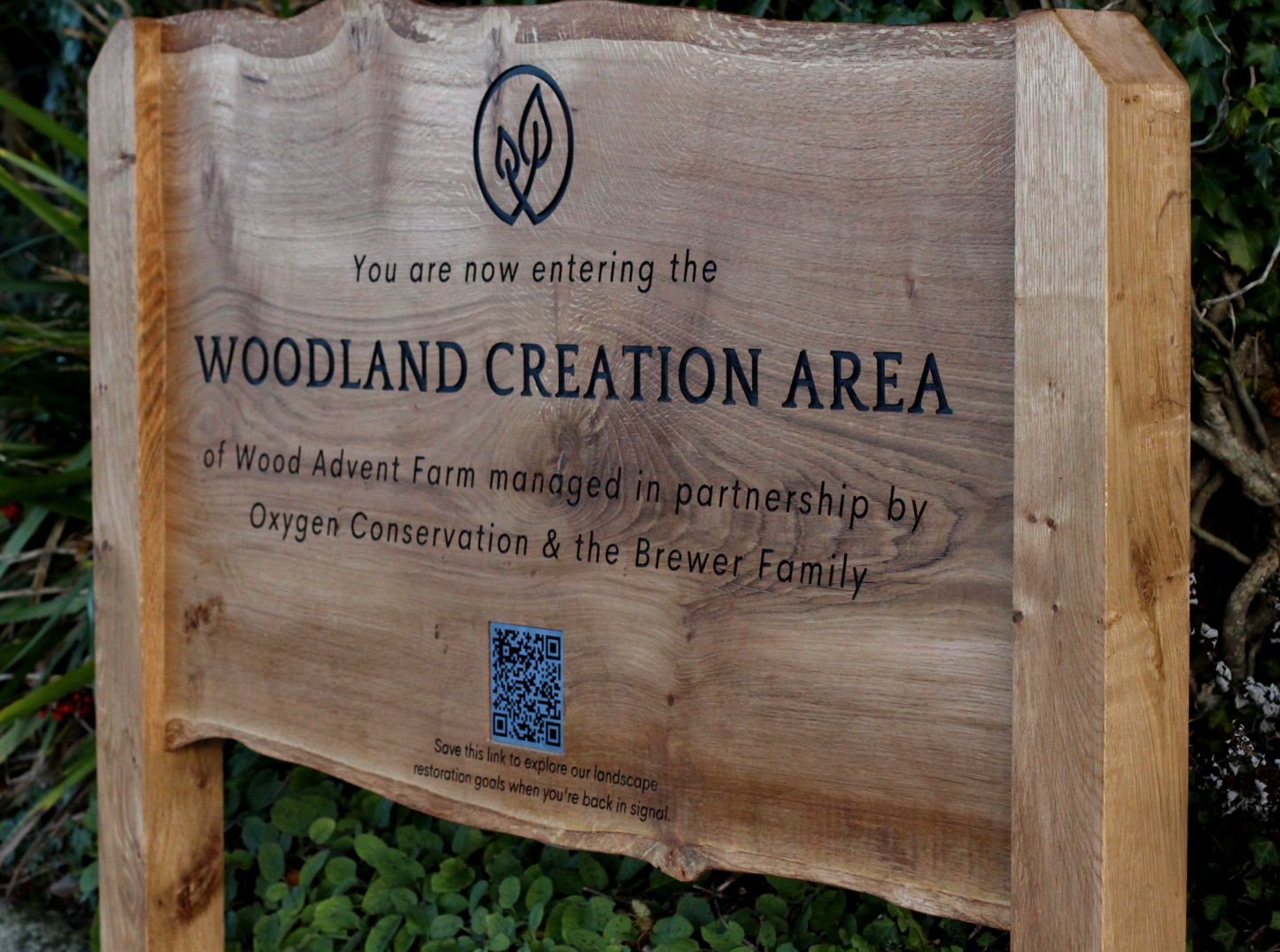 Wooden sign indicating entry to a woodland creation area with text and a QR code.