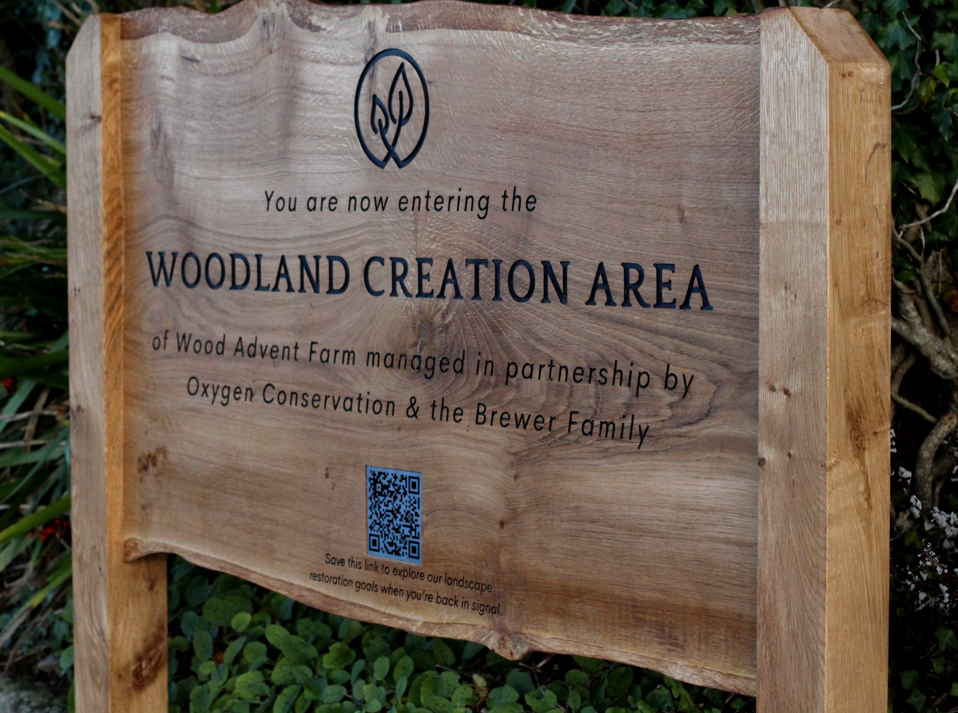 Wooden sign indicating entry to a woodland creation area with text and a QR code.