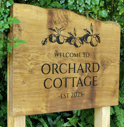 Wooden sign with 'Welcome to Orchard Cottage EST 2025' text and decorative elements in a garden setting.