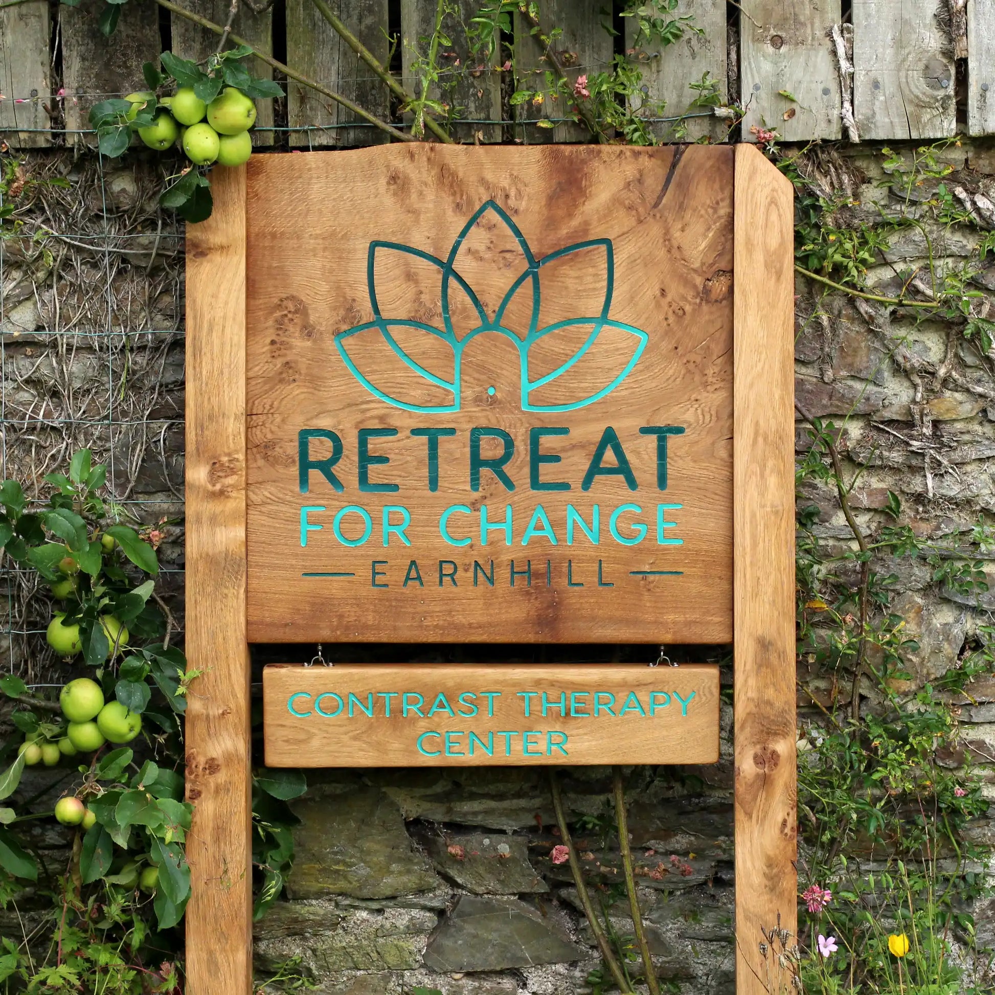 Wooden sign for 'Retreat for Change Earnhill' against a stone wall and greenery background