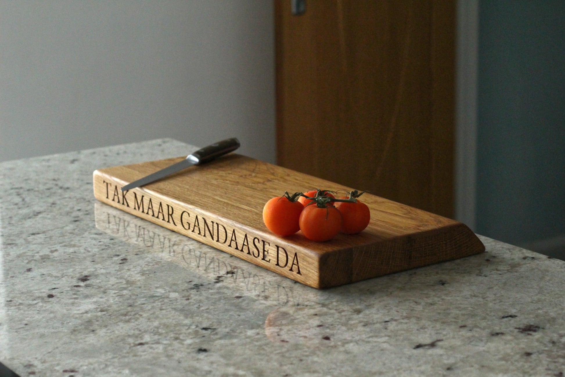 Wooden cutting board with engraved text and a knife on a marble surface
