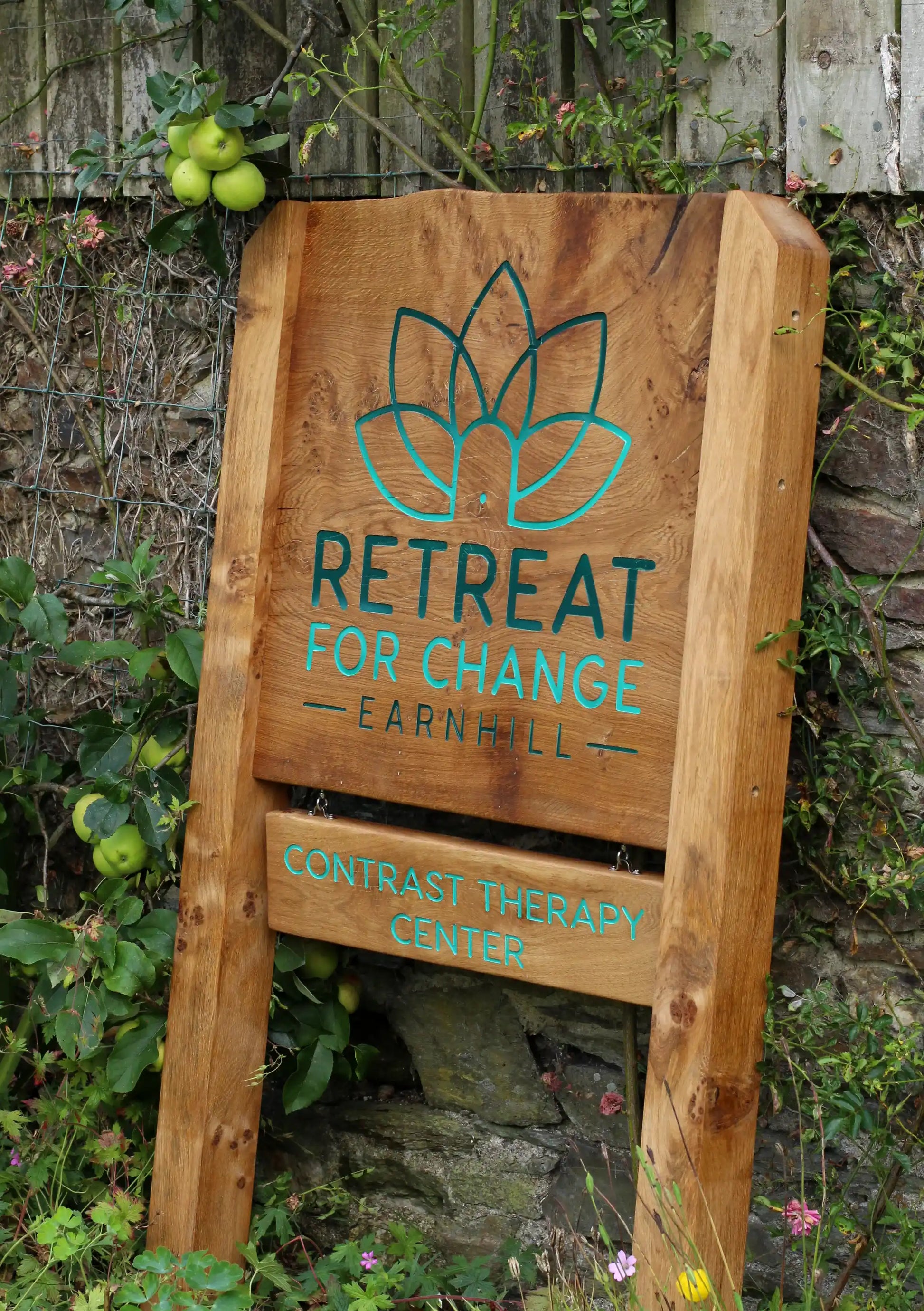 Wooden sign for 'Retreat for Change Earnhill' contrast therapy center with green text and logo.