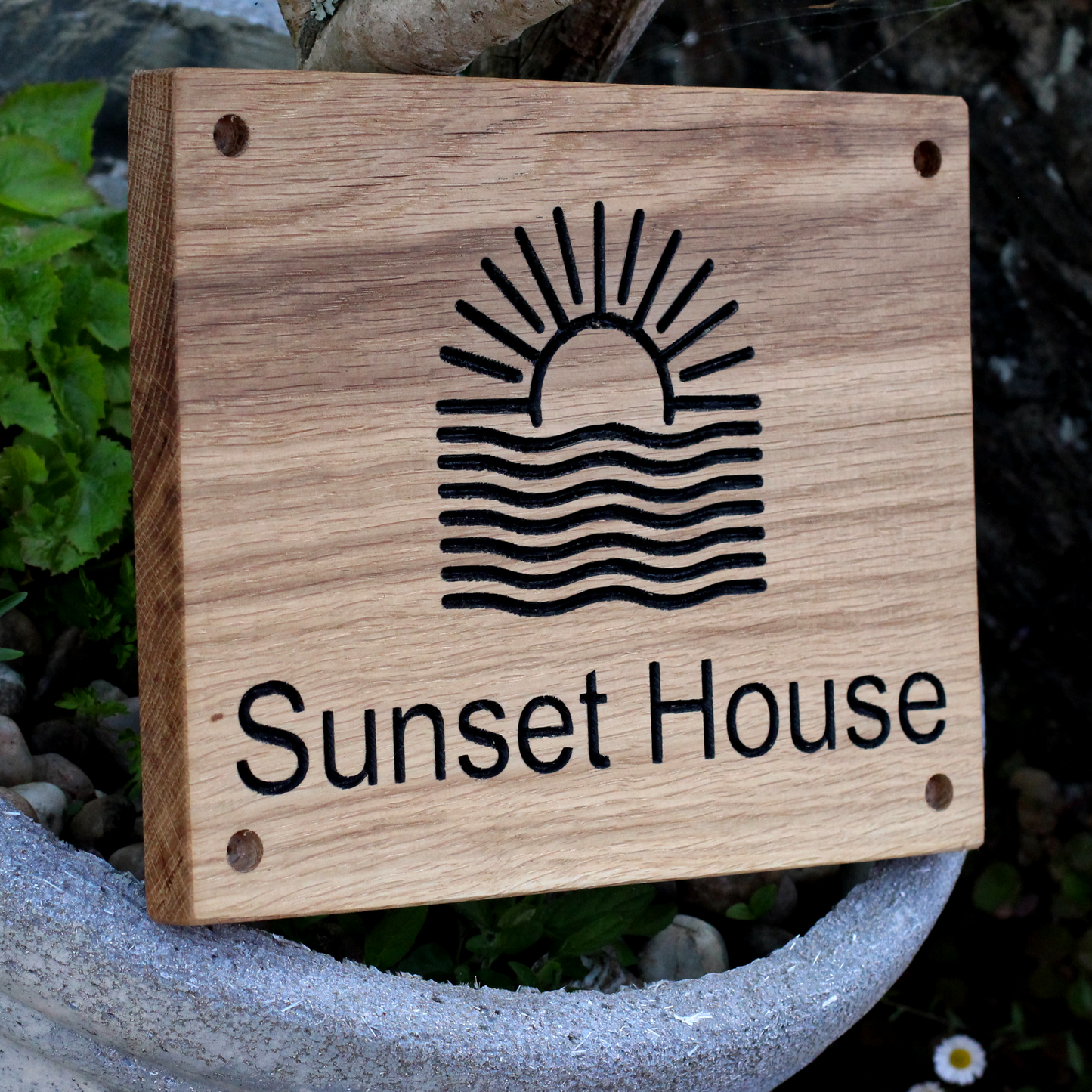 Wooden sign with 'Sunset House' and a sun and wave design, placed outdoors.