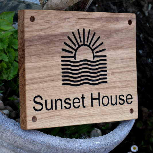 Wooden sign with 'Sunset House' and a sun and wave design, placed outdoors.