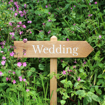 A wooden wedding sign with 'Jess & Olle's Wedding 31.07.2021' engraved on it, set against a backdrop of greenery.