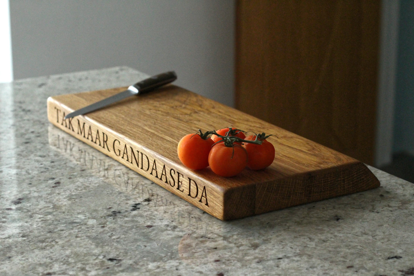 Wooden cutting board with engraved text and tomatoes on a marble surface