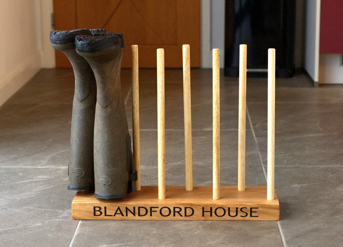 Wooden boot rack with 'Blandford House' branding on a tiled floor.