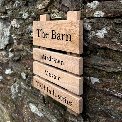 A rustic wooden slat sign reading 'The Barn' with engraved names 'Airdrawn', 'Mosaic', and 'TRH Industries' mounted against a weathered stone wall.