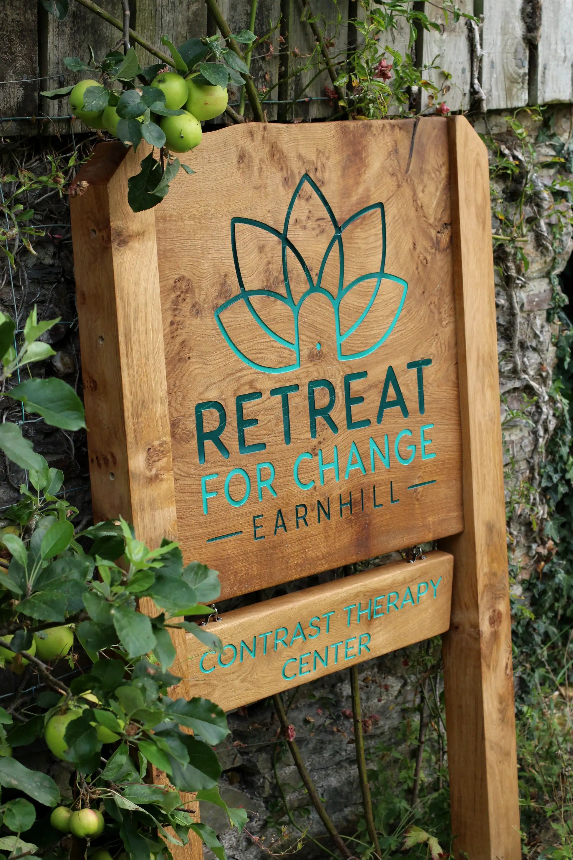 Wooden sign for 'Retreat for Change Earnhill' with green text and logo against a natural background.