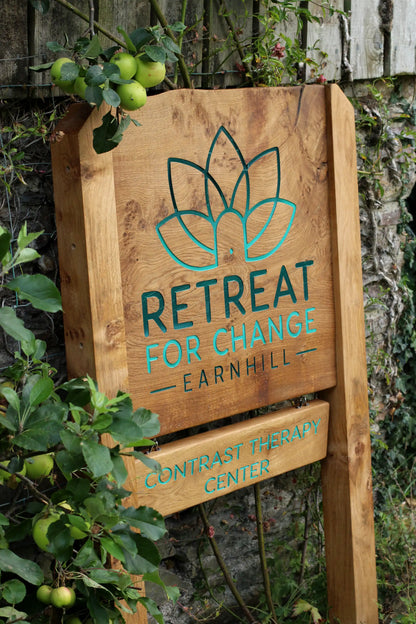 Wooden sign for 'Retreat for Change Earnhill' with green text and logo against a natural background.