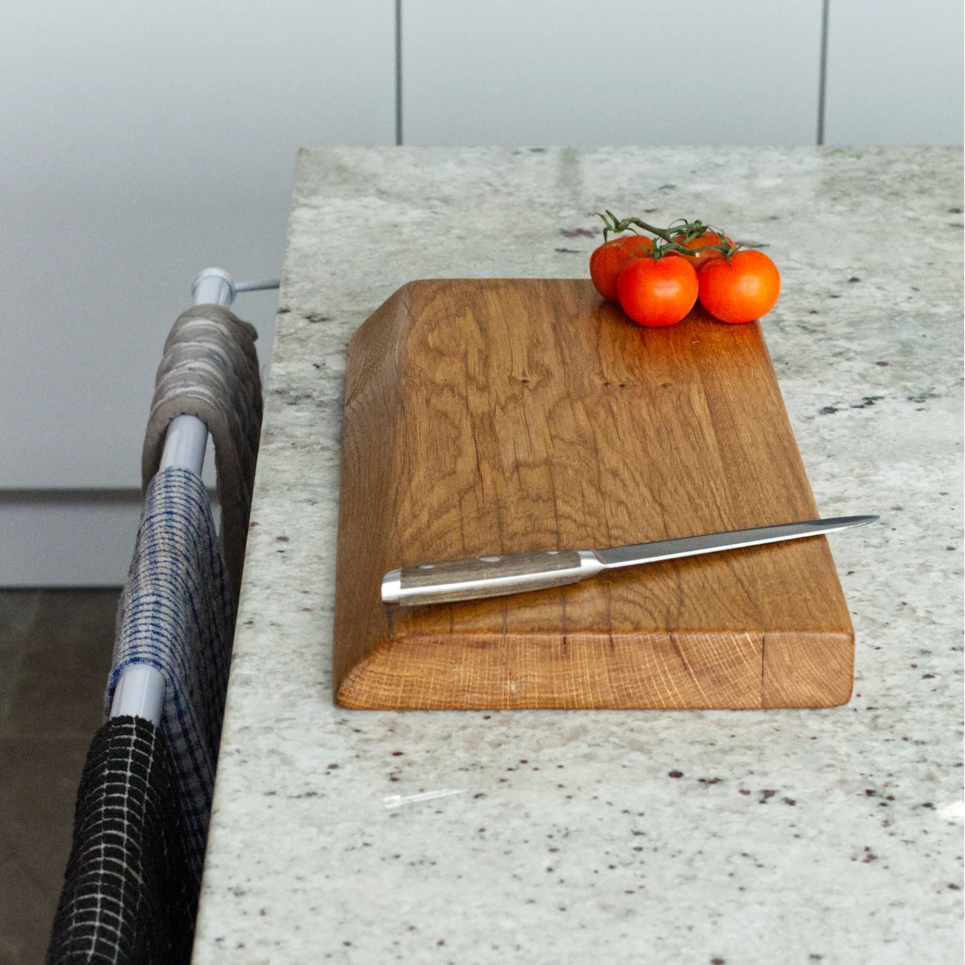 Wooden cutting board with a knife and tomatoes on a kitchen counter