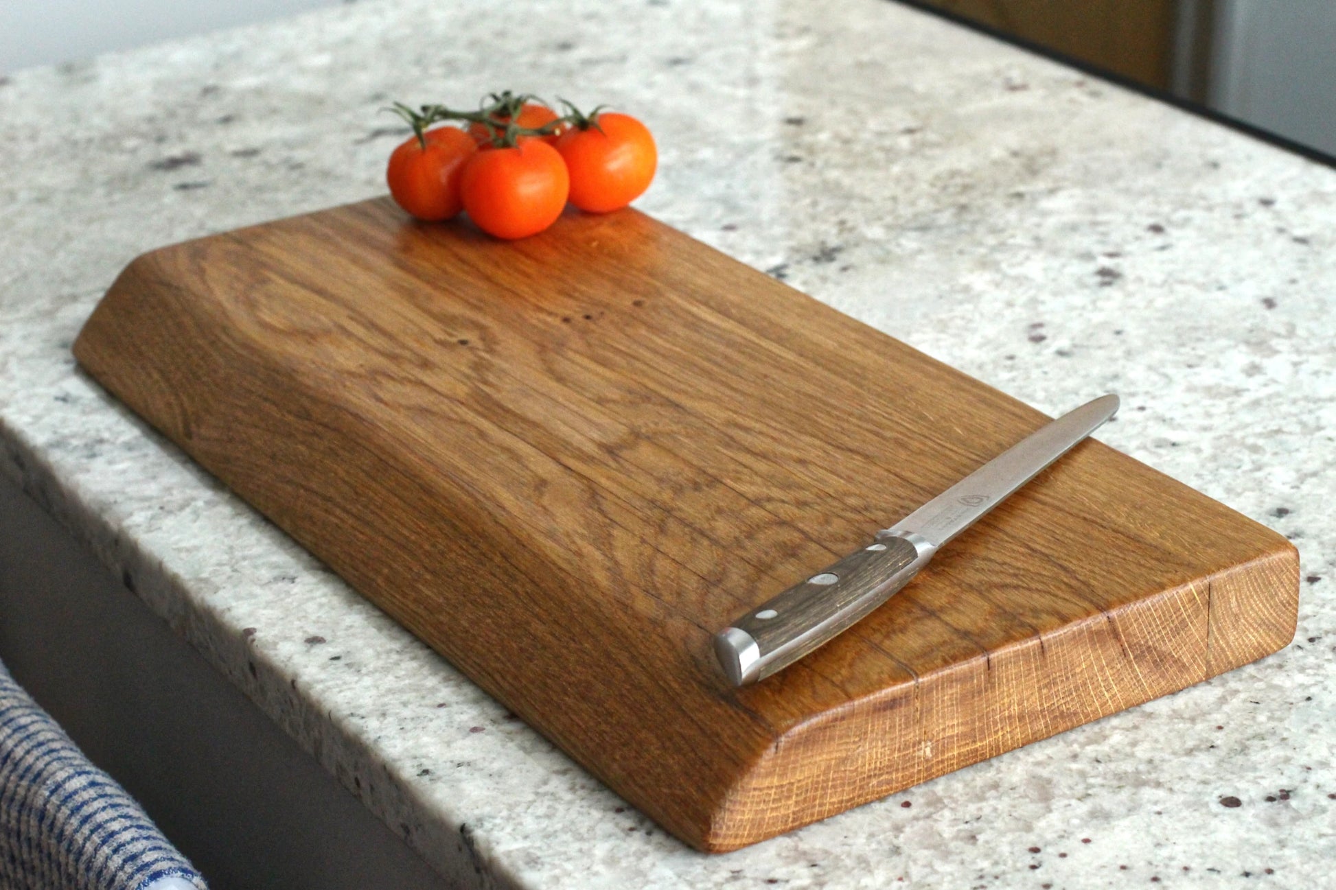Wooden cutting board with a knife and tomatoes on a kitchen counter