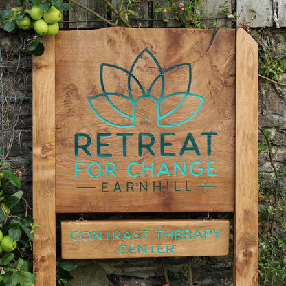Wooden sign with 'Retreat for Change Earnhill' and 'Contrast Therapy Center' text against a stone wall background.