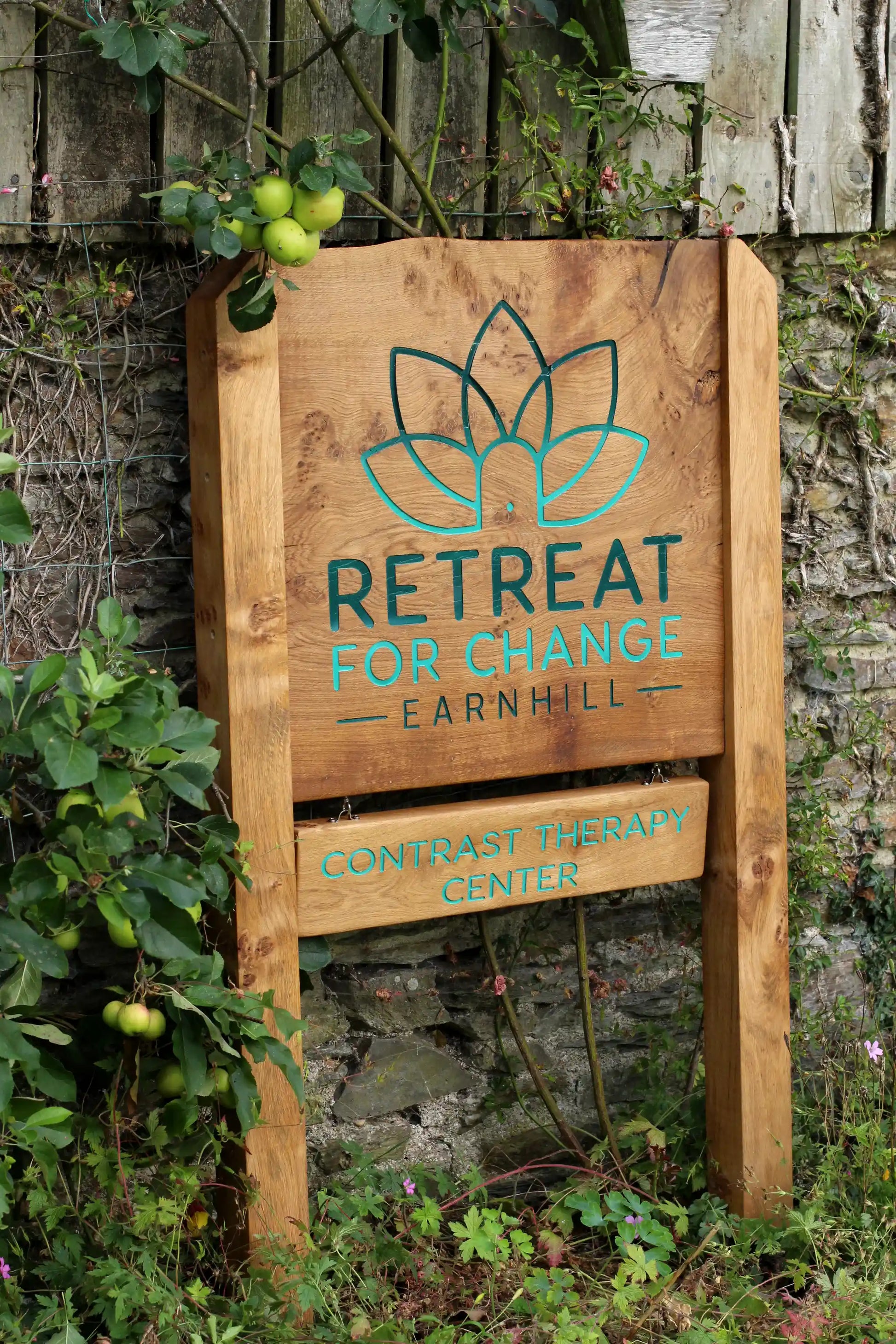 Wooden sign for 'Retreat for Change Earnhill' against a stone wall with greenery.