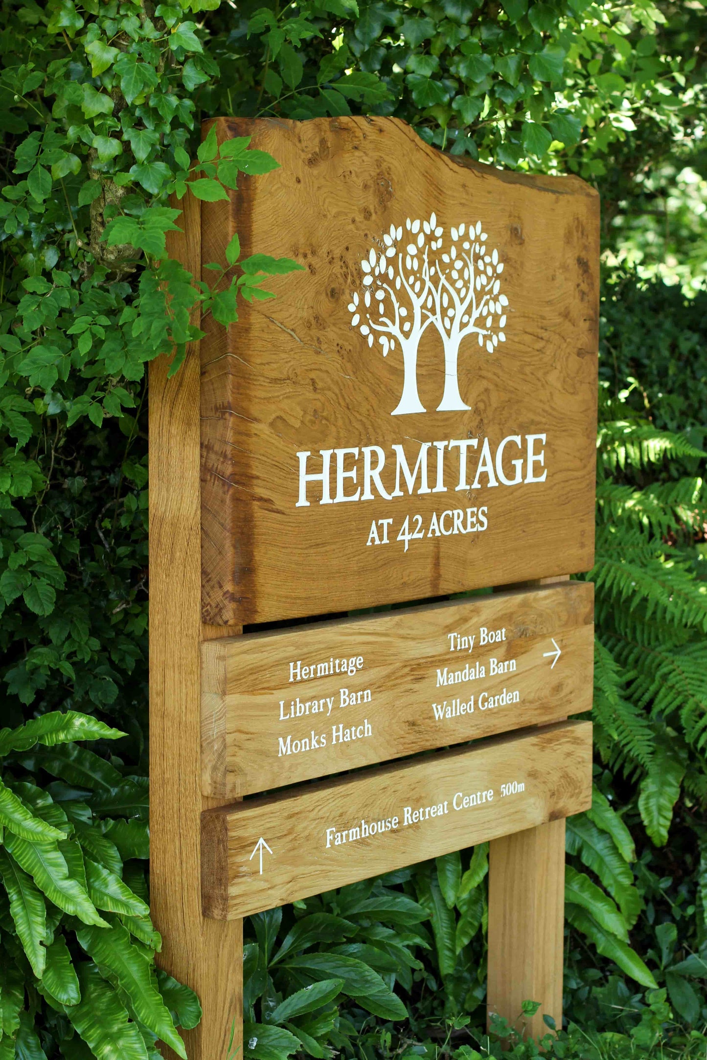Wooden sign with 'Hermitage' and tree logo, surrounded by green foliage