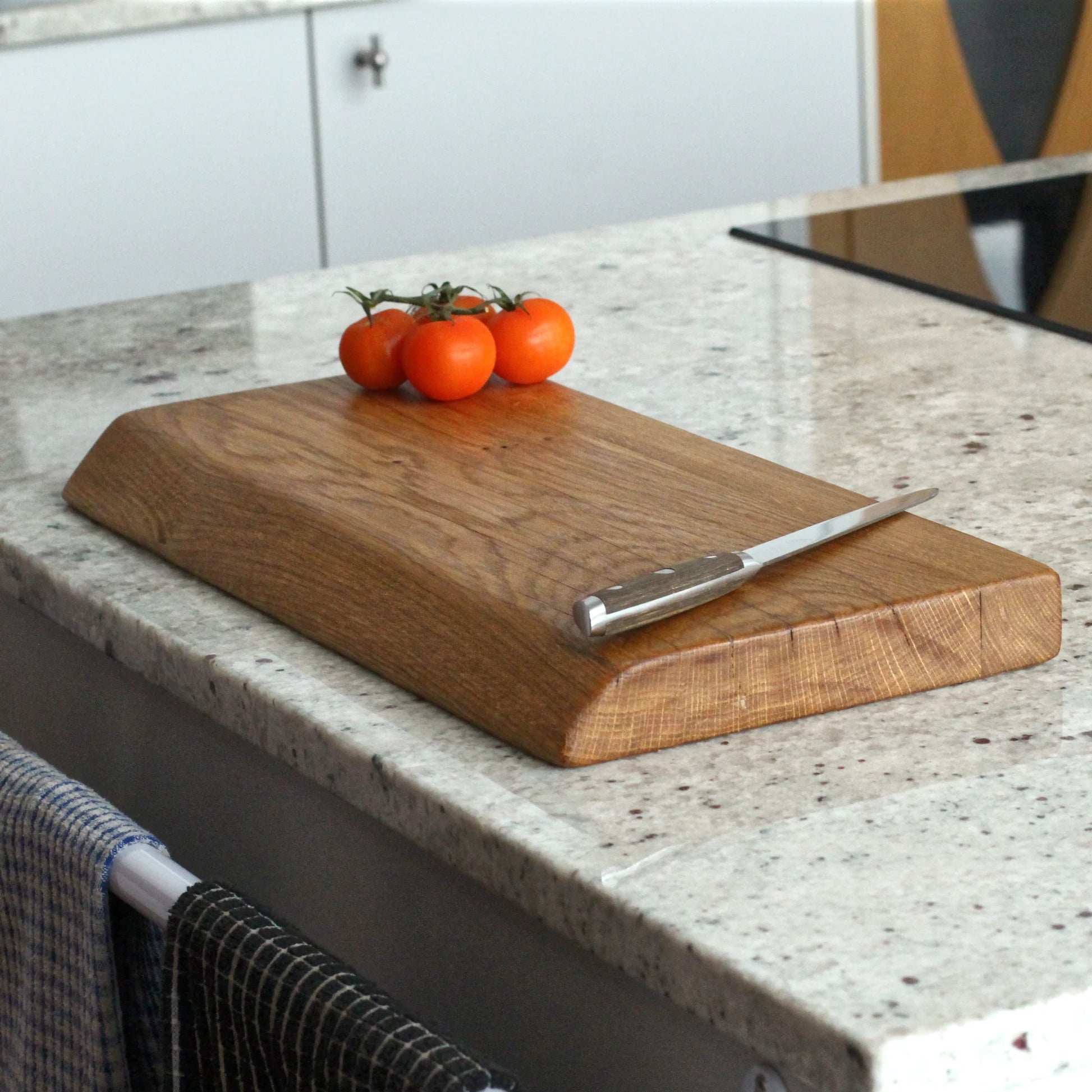 Wooden cutting board with a knife and tomatoes on a kitchen counter