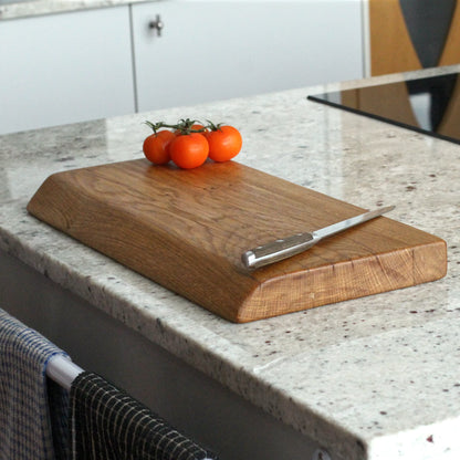 Wooden cutting board with a knife and tomatoes on a kitchen counter