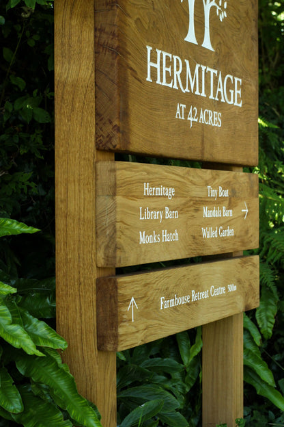 Wooden signpost with directions at Hermitage at 42 Acres, surrounded by greenery.