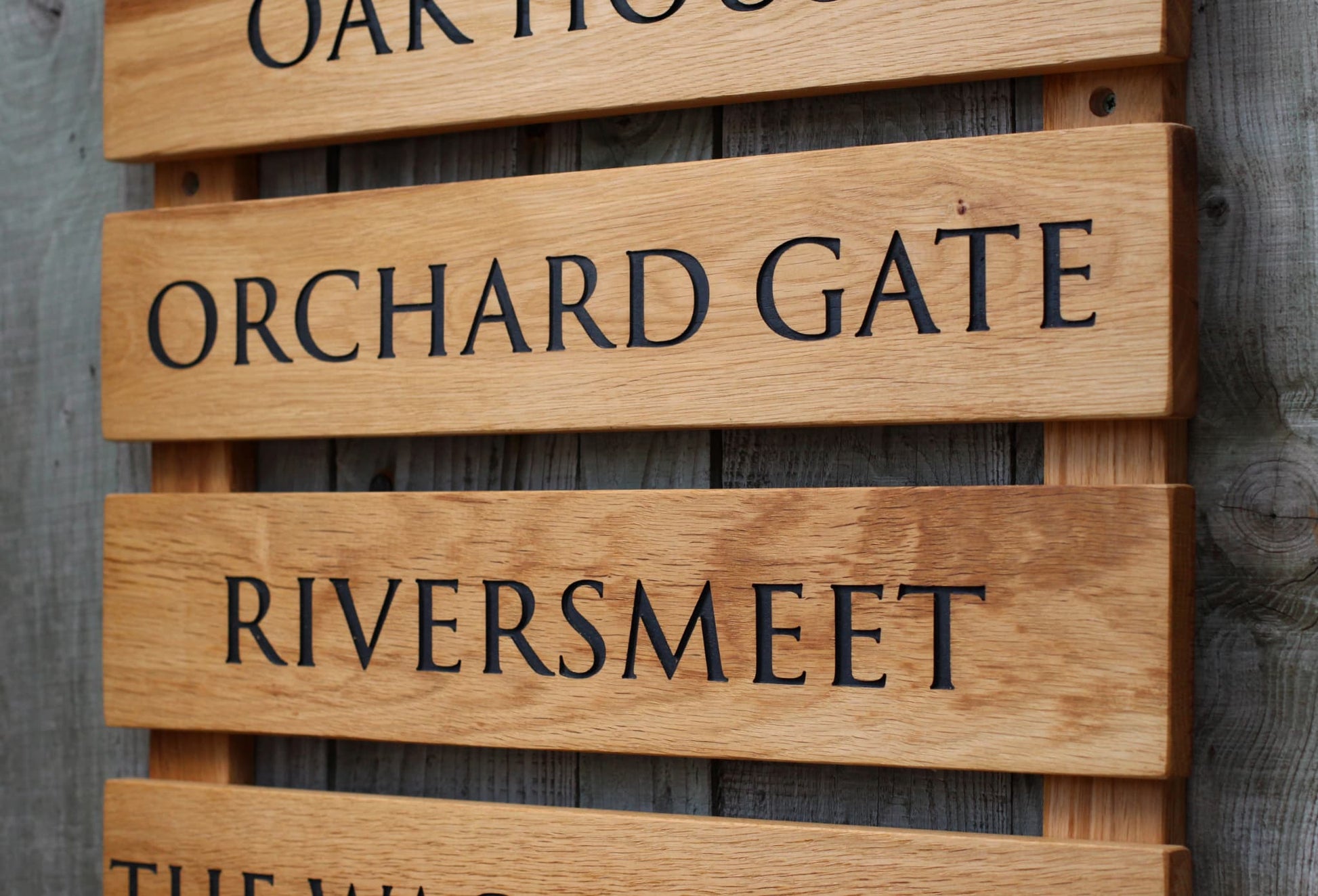 Wooden sign with engraved text 'Orchard Gate Riversmeet' on a wooden background
