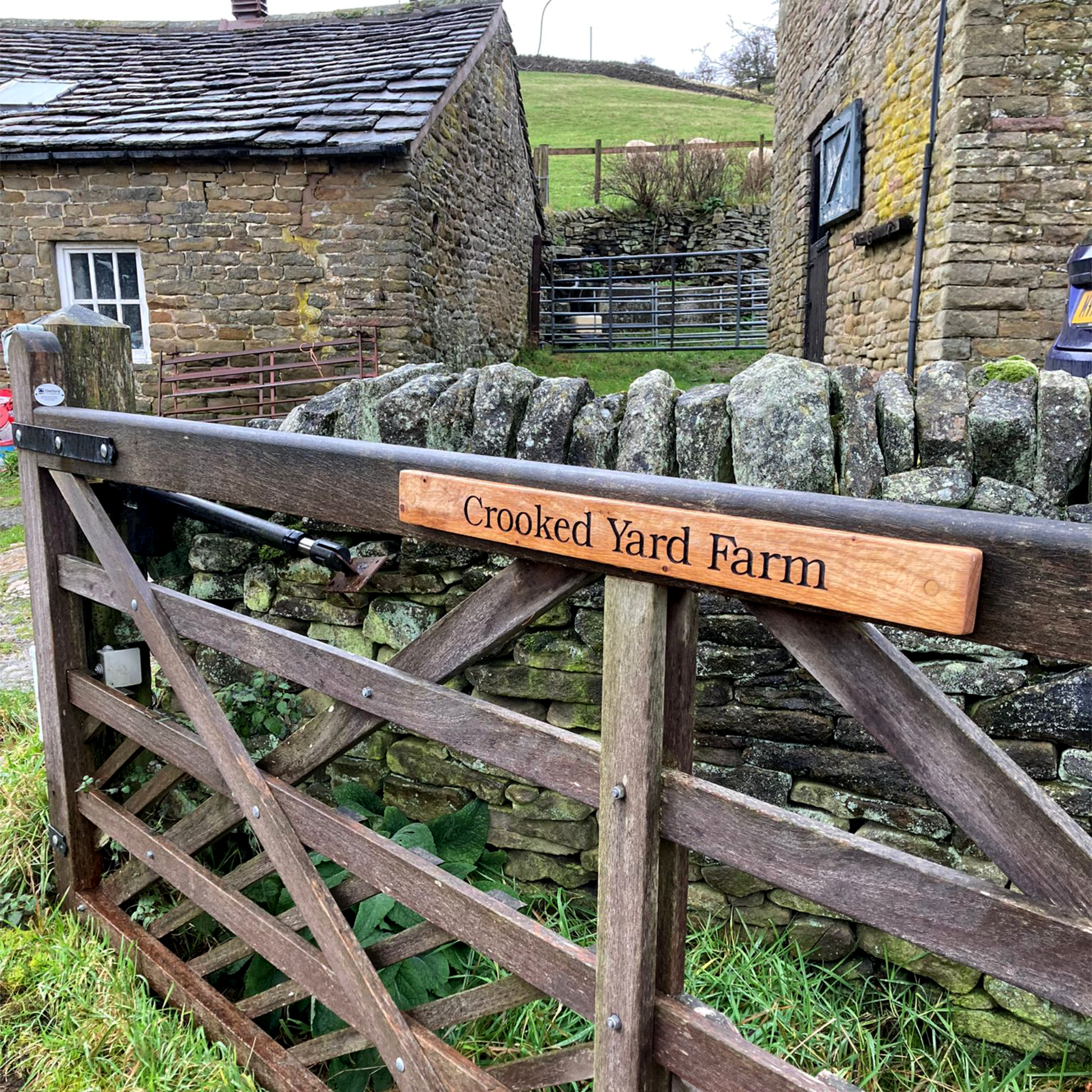 Wooden gate with 'Crooked Yard Farm' sign in front of stone buildings and a stone wall.