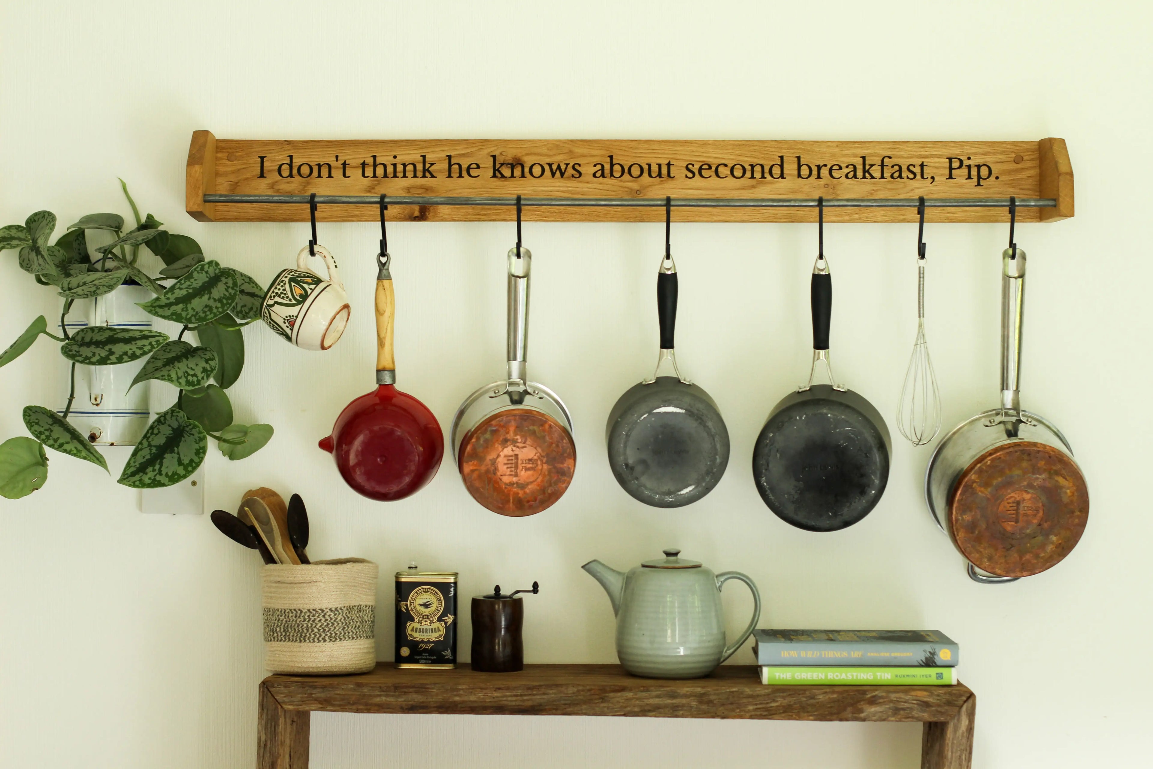 Hanging pots and pans on a wooden rack with a quote above, against a white wall.